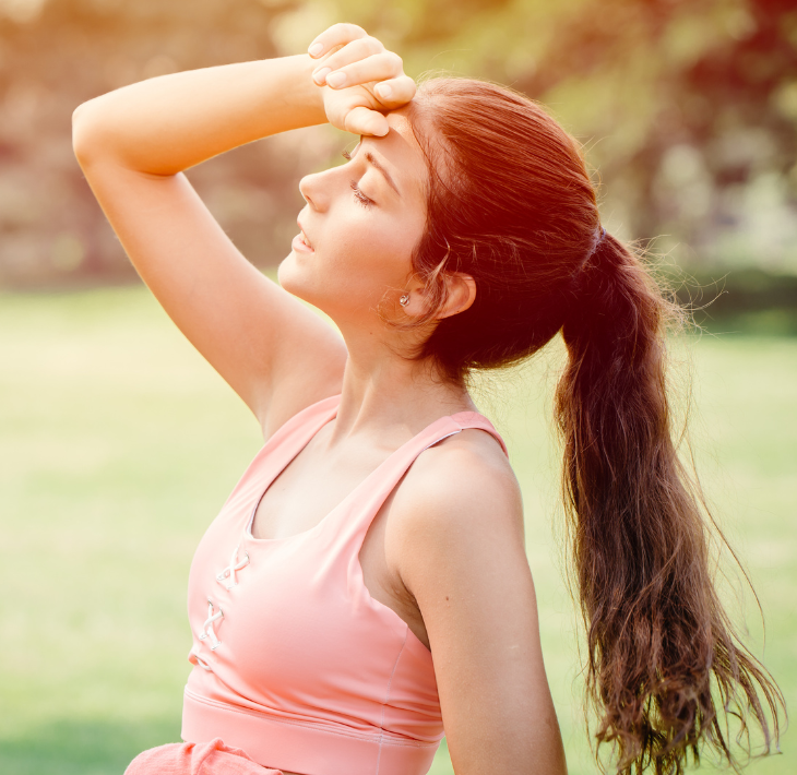 A woman wearing her extensions in a ponytail presses a hand to a sweaty forehead