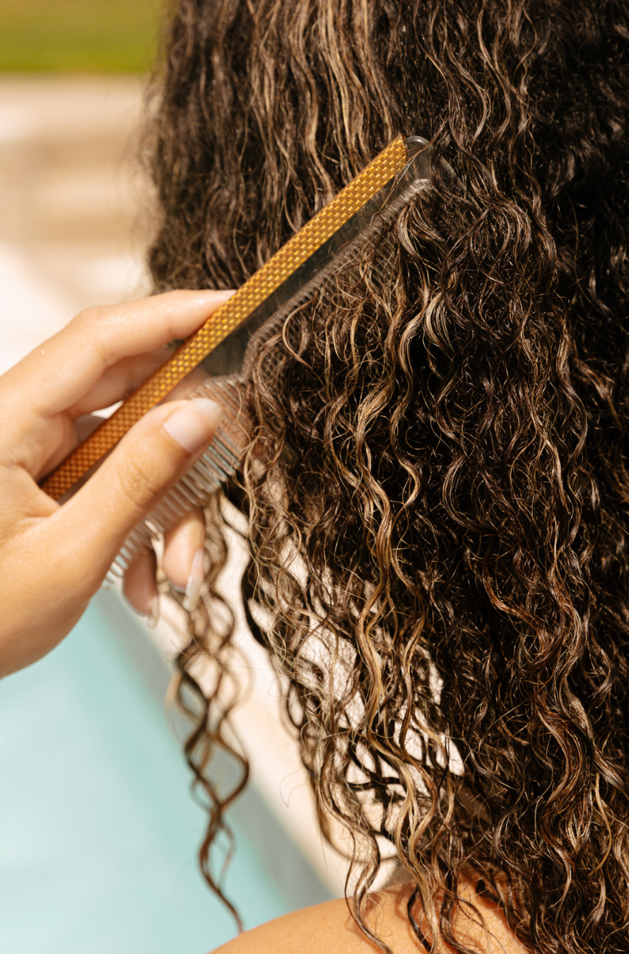 A woman combs leave-in product into her extensions by the pool