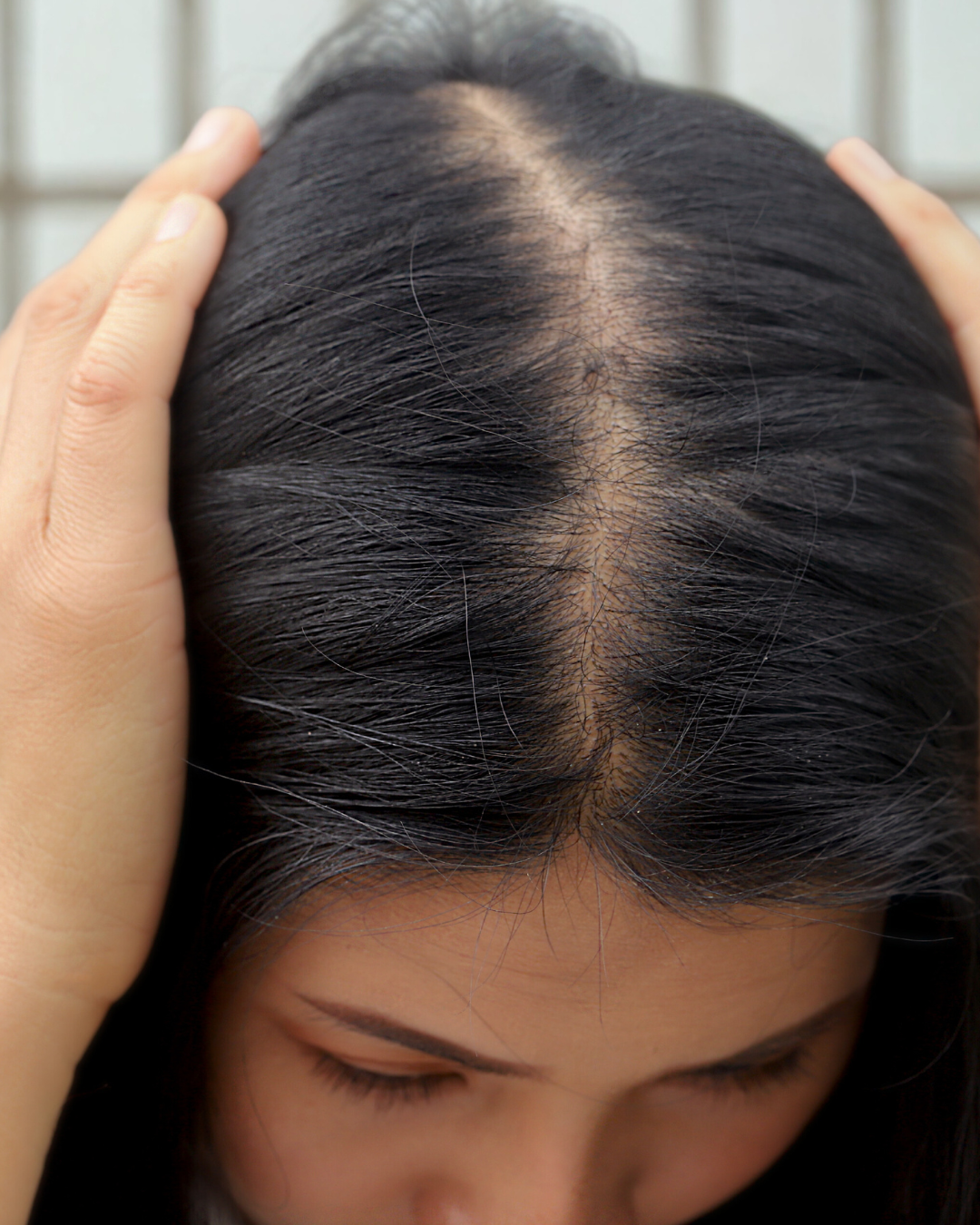 a woman examines her widening part due to hair thinning